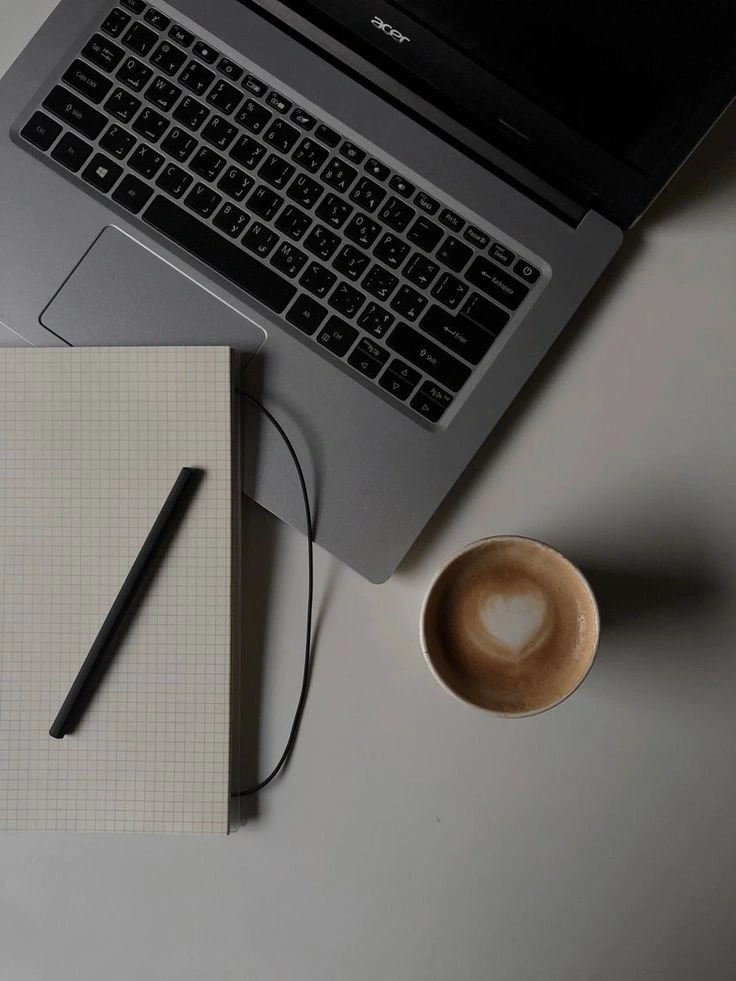 Overhead shot of a laptop, notebook, pencil, and a coffee cup with a heart design. Workplace of the Best Freelance Digital Marketer in KannurKerala